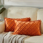 Orange textured pillows with pom-pom trim on a beige sofa.