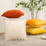 Decorative pillows with pom-pom trim on a surface with a plant in the background