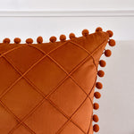 Orange pillow with diamond pattern and pom-pom trim on a white background