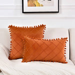 Two orange textured pillows with pom-pom details on a white couch.